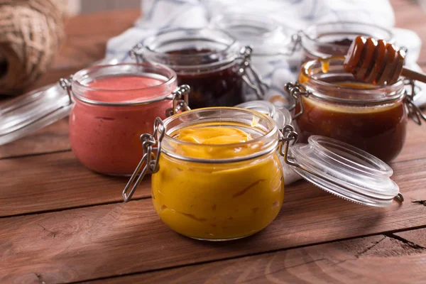 Ahşap bir masa üzerinde bir küçük cam kavanoza doğal kremler. Karamel, mango, çilek, berry, çikolata sosu