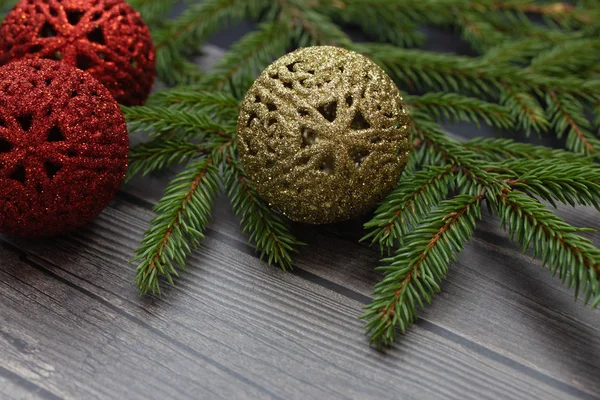 Red and gold Christmas balls with green spruce on a gray wooden background close-up. Christmas toy.