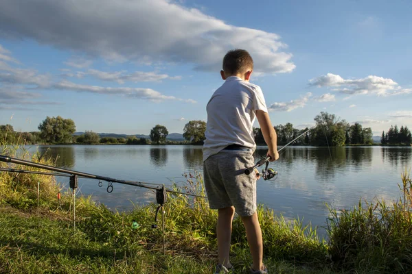 View on boy fishing on a lake from behind. Beautiful fish pond in Badin, near Banska Bystrica, Slovakia. Child holding fishing rod and catching fish. Little fisherman.