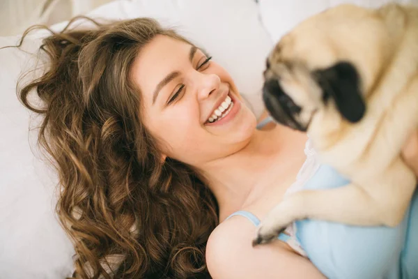ベッドで彼女のパグ犬を抱いて愛らしい女性 — ストック写真