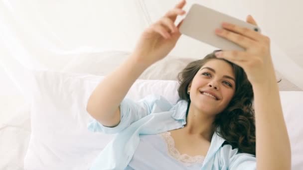 带着自拍与手机聊天美丽的年轻微笑的女人在床上 — 图库视频影像