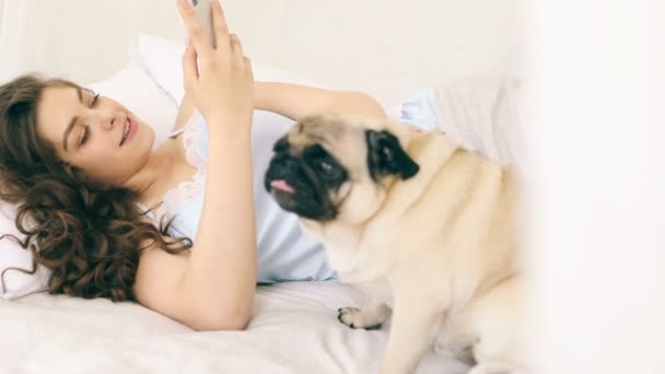 Redes sociales de telefonía móvil usando en la cama. Una mujer con un perrito raro. Imágenes de video. Fin de semana soleado — Vídeo de stock