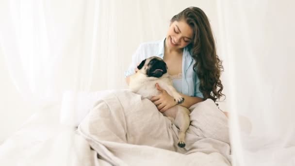 Pizsama játszik vele kutya az ágyban vonzó nő. Videofelvétel. Nyári időszámítás — Stock videók