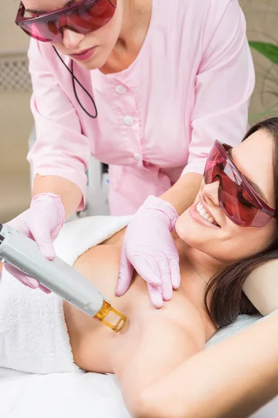 Mujer cliente feliz teniendo procedimiento de depilación láser de la axila. Servicio profesional de belleza de la piel en proceso . — Foto de Stock