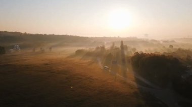 Gündoğumu ve sis ile yol boyunca kırsal bir otobüs sürmek. Sahne kırsal panorama manzara. Dron aeriel video görüntüleri.