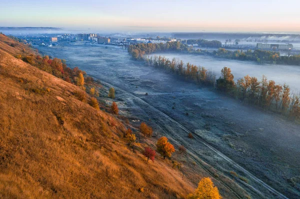 Hösten torrt gräs hill och dimmig blå dalen. Soluppgång. Staden i bakgrunden. — Stockfoto