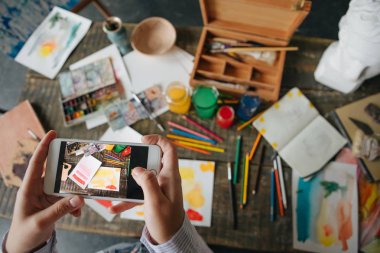 Internet üzerinde sanat eseri ile fotoğraf paylaşımı. El tutma telefon ve sanat eseri resimlerini vardır. Yukarıdan sanatçılar Resepsiyon Masa üstten görünüm