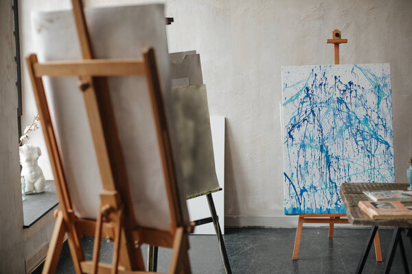 a picture of the artist with splashes of blue paint in the workshop on the easel.