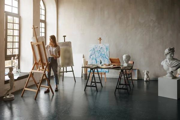 Artista al processo di lavorazione. Giovane donna che crea il dipinto. Sala laboratorio con busti di scultura leggera e classica. Ispirazione atmosfera umore. Retroilluminazione — Foto Stock