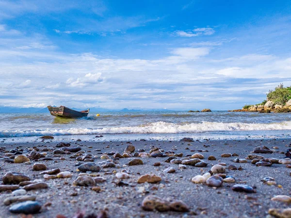 Рыбацкая лодка стоит у берега. голубая вода, небо и камни на переднем плане — стоковое фото