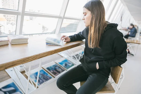 Schwarzes Kapuzenmädchen in hellweißem Café. herrlich entspannte Stimmung. Zeit für Hobby. — Stockfoto