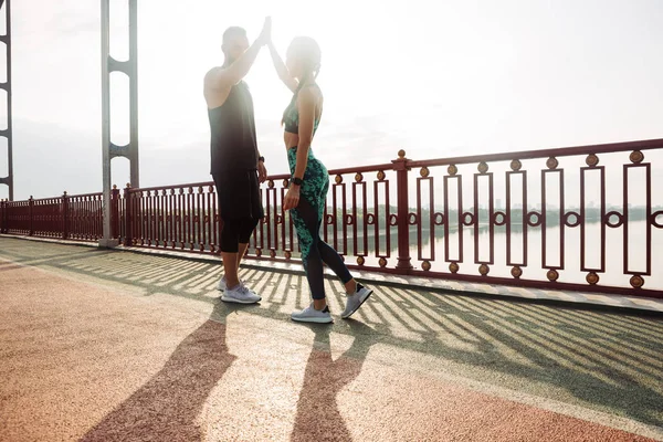 Team work. Active couple high five after workout marathon. Good result, reach the goal. Sport outdoors on the bridge