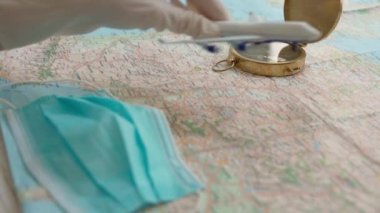 seyahat acentası teması. Virüs koronası karantinası sırasında kişisel koruma malzemelerini maske ve tıbbi eldivenlerle planlamak. Uçak kalkmak üzeredir. Harita, pusula, yüz maskesi, turizm videosu