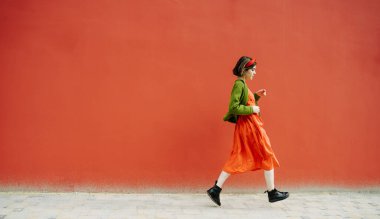 Kırmızı arka planda koşan güzel aktif genç kız. Kırmızı elbise ve yeşil ceketle şık bir renk kombinasyonu. Aktif yaratıcı genç kadın. Boşluk. Sanatsal trendler. üretim sorunları