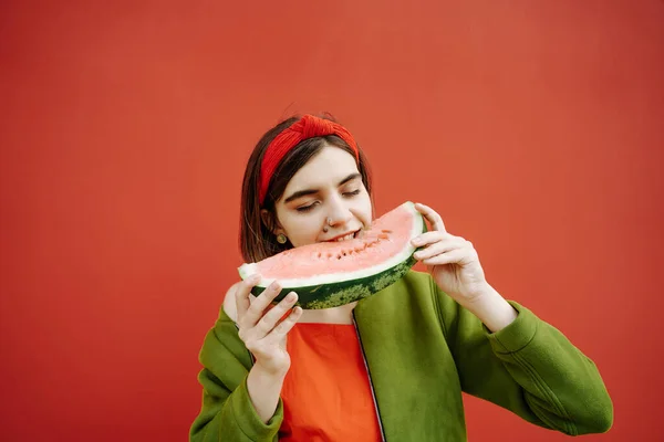 西瓜吃甜水果 年轻美丽的女孩穿着红色衣服和绿色夹克 时尚时尚概念的构图 红墙背景 鲍勃剪头发和流行配饰风格的心情 — 图库照片