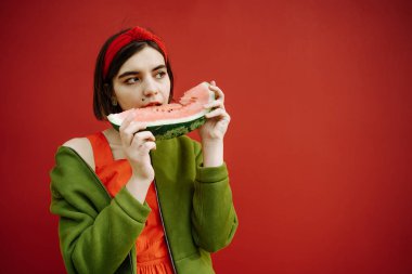 Yeşil ceketli, karpuz dilimli, şık esmer kız yemekten zevk alıyorum. Tatlı zamanı tatlı zamanı. Güzel, genç bir kız ilgisiz görünüyor. Parlak kavramsal ifade kompozisyonu.