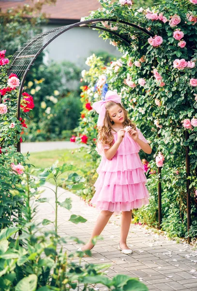 在玫瑰园里 穿着粉色连衣裙头带蝴蝶结的女孩 女娃娃 — 图库照片