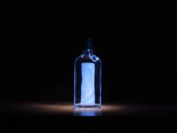 Transparent glass bottle with a label on the light on a black background — Stock Photo, Image