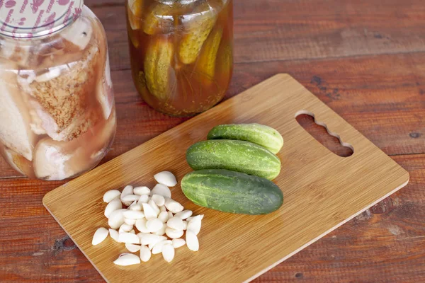 Cetrioli chiusi e lardo chiuso con carne in barattoli di vetro per l'inverno. Tagliere con cetrioli e fette di aglio — Foto Stock