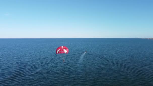 Fallschirmspringen mit dem Boot, extreme touristische Unterhaltung, Erholung und Freizeit auf See, Luftaufnahme. Schöne Landschaft des blauen Meeres, die mit dem Horizont des blauen Himmels verschmilzt — Stockvideo