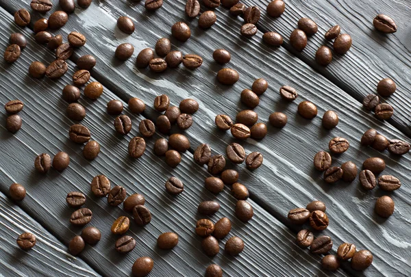 Kahve çekirdekleri gri ahşap bir masanın üzerinde yatar. Kahve çekirdeklerinin arkaplan dokusu