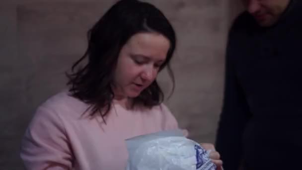 Чоловік дарує новорічний подарунок молодій збудженій жінці, що стоїть біля ялинки вдома — стокове відео