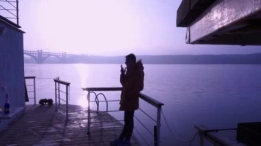 Sarı ceketli adam sigara içiyor. Günaydın, nehir, sis, Doğa, kayalar. Su üzerinde ev.