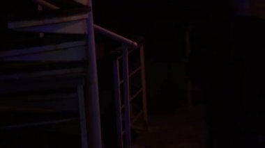 Bir adam dairesel merdivenden geçiyor. Evin köşesinden geliyor. Gece. Su üzerinde ev, gece lambaları.