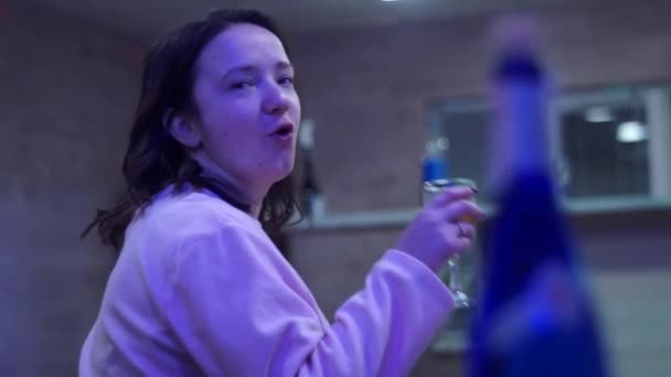 Het meisje drinkt wijn van een glas, zoals wodka. Een feestje. Op de voorgrond een fles. — Stockvideo