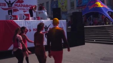 Genç erkekler ve kızlar maratondan sonra, koşudan sonra, Zaporozhye 'de, yorgun, Holi boyası içinde, dinlenmek için merdivenlerden yukarı çıkarlar. 27 Nisan 2019. Kel bir adamın kafası ve kıyafetleri sarı ve kırmızıydı.