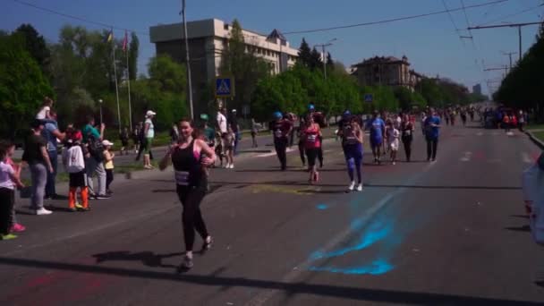 Tres jugadores corren en forma de rugby, fútbol americano. Mucha gente, niños corren una maratón a lo largo de la carretera, a lo largo de la avenida, a lo largo del asfalto, en la pintura de holi, en diferentes colores, en — Vídeos de Stock