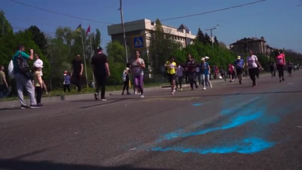 Wiele osób biegać maraton wzdłuż drogi, wzdłuż alei, wzdłuż asfaltu, w farbie Holi, w różnych kolorach, w Zaporoże. Na asfalcie, Holi, żółty i niebieski. Szczęśliwy śmiech w tle — Wideo stockowe