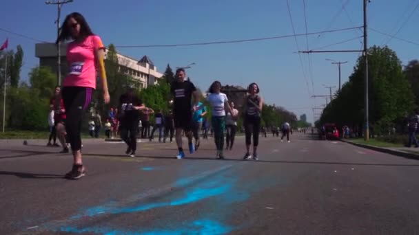 Een heleboel mensen lopen een marathon langs de weg, langs de laan, langs het asfalt, in Holi Paint, in verschillende kleuren, in Zaporizhia. Op asfalt, Holi, geel en blauw. Drie jonge jongens lopen — Stockvideo