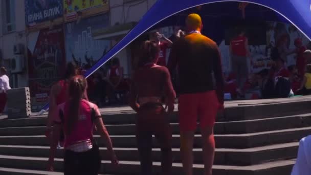 Young boys and girls after the marathon, after running, in Zaporozhye, tired, in the paint of holi, go up the stairs to rest. April 27, 2019. A bald guy has all his head and clothes in yellow and red — стокове відео