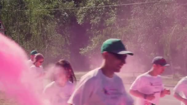 Les organisateurs jettent, jettent de la peinture holi, rose, couleur, au visage des coureurs de marathon qui courent le long de l'avenue, sur la route asphaltée en t-shirts blancs, casquettes, lunettes de soleil et couvrir le nez avec son — Video