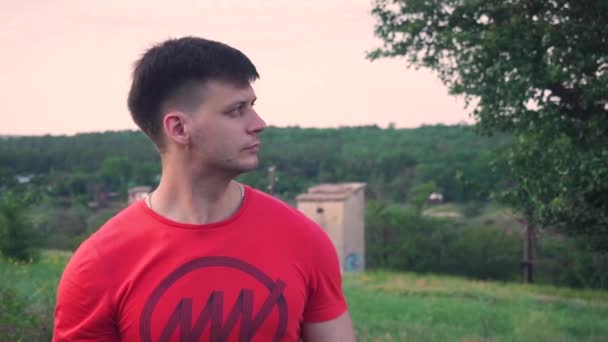 Gros plan gars, T-shirt rouge fond d'arbre vert, détourner les yeux, dans la caméra, sourire — Video