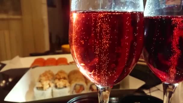 Close-up rising bubbles in glass with red champagne, table with sushi, rolls on background — Stock Video