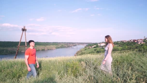 Après un baiser, un bel homme et une femme rient et s'amusent au centre du cadre, un pont, une rivière, des arbres, de l'herbe, des maisons sur fond de plan général , — Video