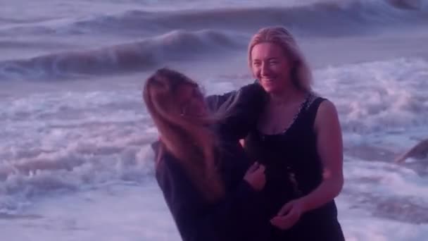 Mamma e figlia abbracciano, ridono, sorridono, sullo sfondo del mare, grandi onde, schiuma, spiaggia — Video Stock