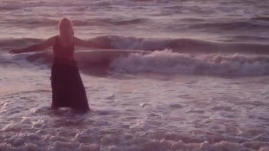 Siyah elbiseli mutlu kadın denizde duruyor, kolları yana uzatılmış.