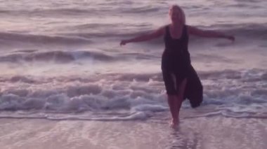 Siyah bir elbise kadın onun tarafında kucaklamak için kollarını yaymak için çalışır, deniz, büyük dalgalar