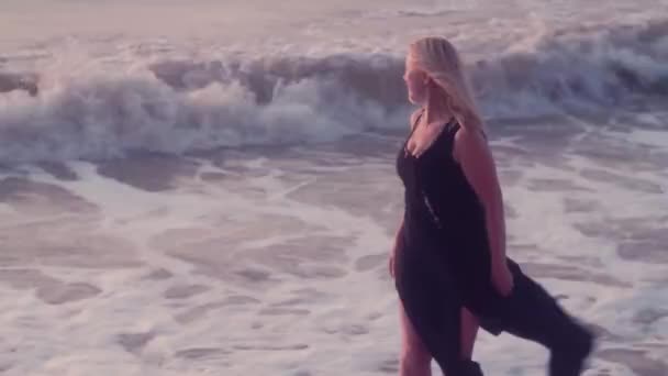 Женщина в черном платье бежит к своей стороне, раскидывая руки, чтобы обнять, на море, большие волны — стоковое видео