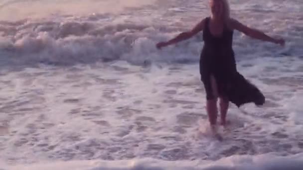 Femme en robe noire court sur le côté écartant les bras pour embrasser, sur la mer, de grosses vagues 
