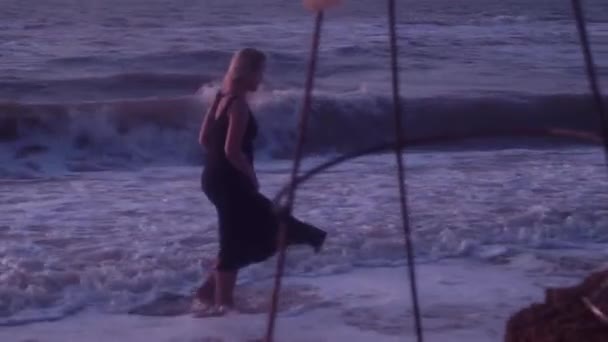 黒いドレスを着た女性は、海水、波、泡で、ビーチを歩きます。石、土、粘土で通り過ぎる — ストック動画