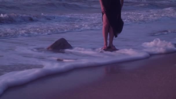 Γυναίκα με μαύρο φόρεμα στέκεται πάνω σε μια πέτρα στα κύματα, αφρός, καλοκαίρι, βράδυ — Αρχείο Βίντεο