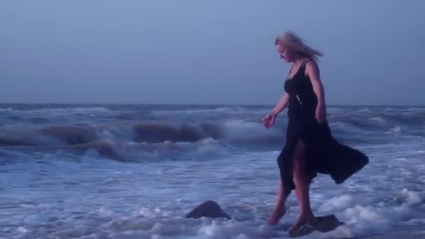 女性は、片足の石の上に立って、海で、落ちて、笑い、彼女のバランスを保とうとします — ストック動画
