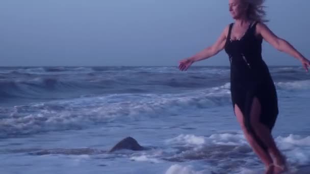 Vrouw loopt weg van de golven, het schuim van de zee, op het strand in winderig weer — Stockvideo