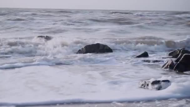 Golven bedekken de graniet zwarte stenen in de zee tegen de hemel — Stockvideo