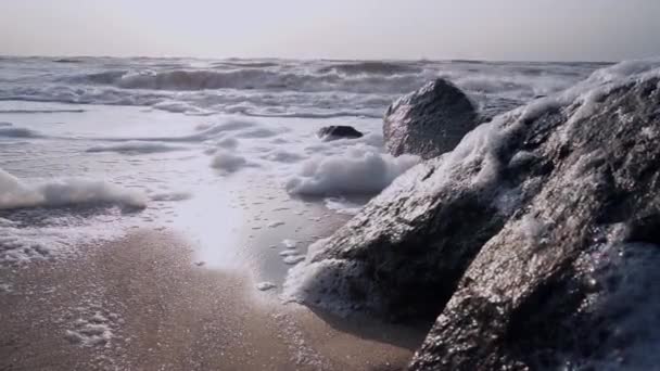 Fale surf z pianki zbliża się do kamery w pobliżu czarnego kamienia — Wideo stockowe