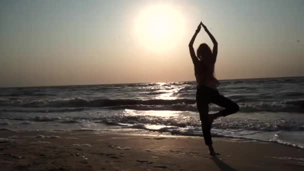 Дівчина стоїть в позі йоги, навпроти сонця на заході сонця, на пляжі, на морі — стокове відео